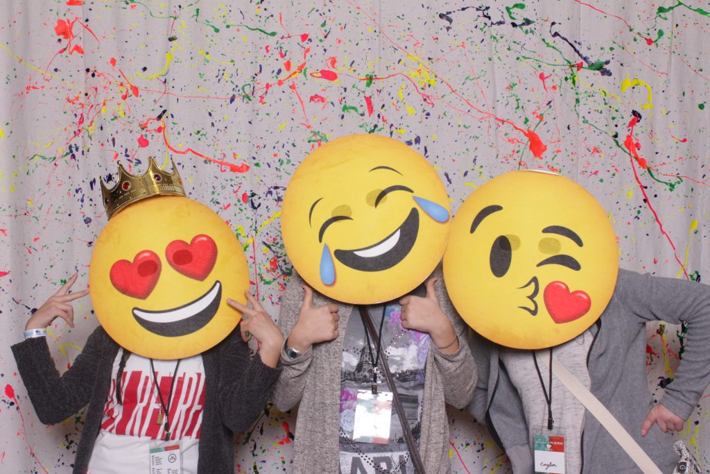 Girls taking a picture in a photo booth with emoji props at a conference in Toledo