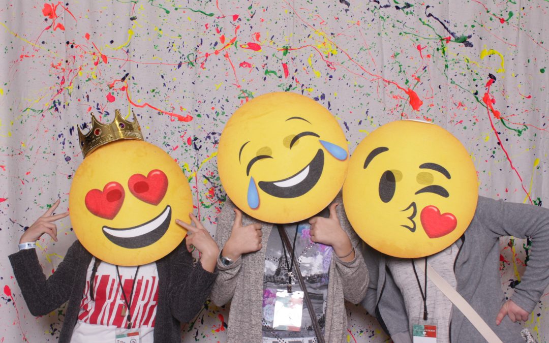 Girls taking a picture in a photo booth with emoji props at a conference in Toledo