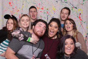 Group of people at an event in a photo booth with a paint splatter backdrop